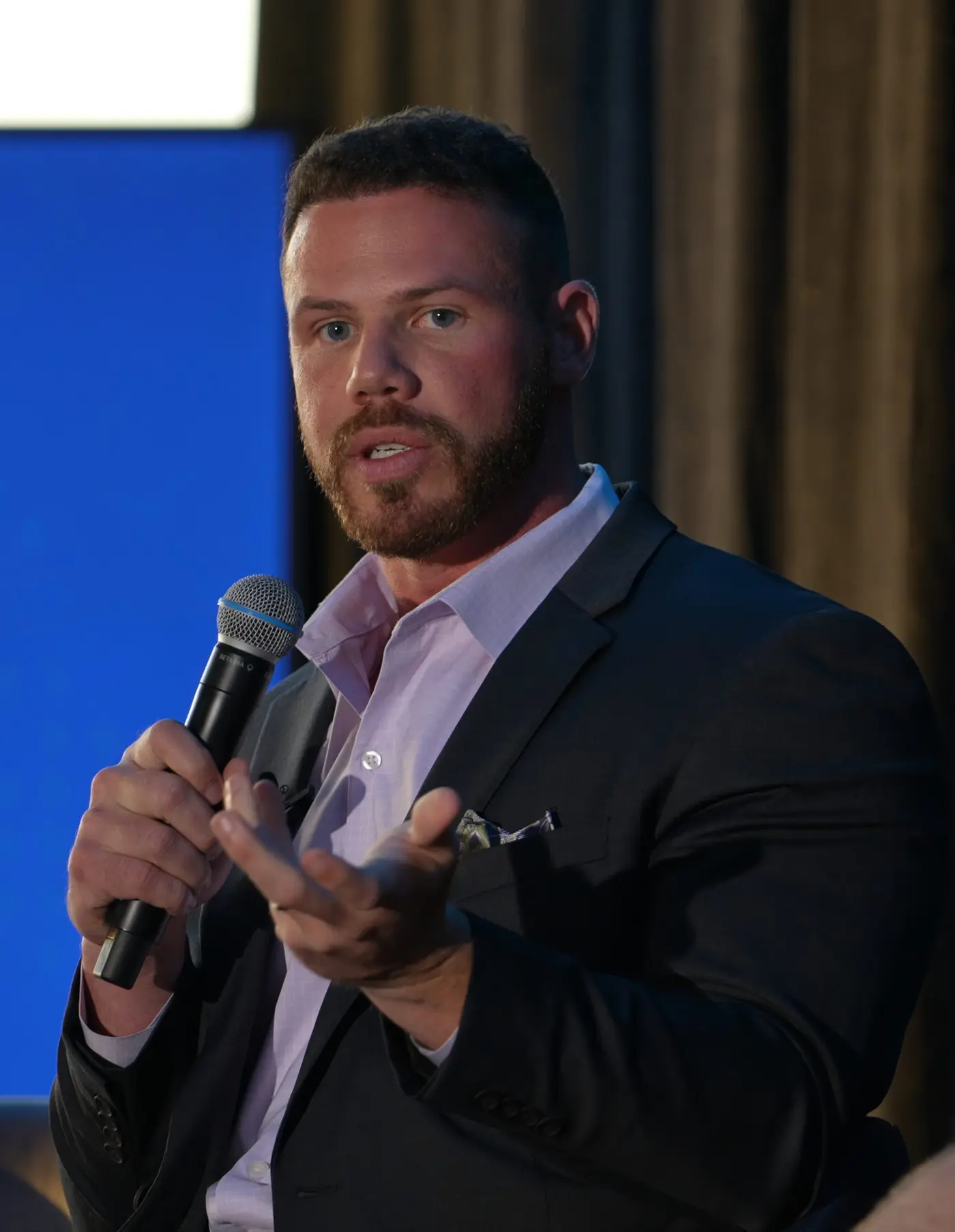 Jake Claver speaking into a handheld microphone on stage at the Digital Fusion Summit
