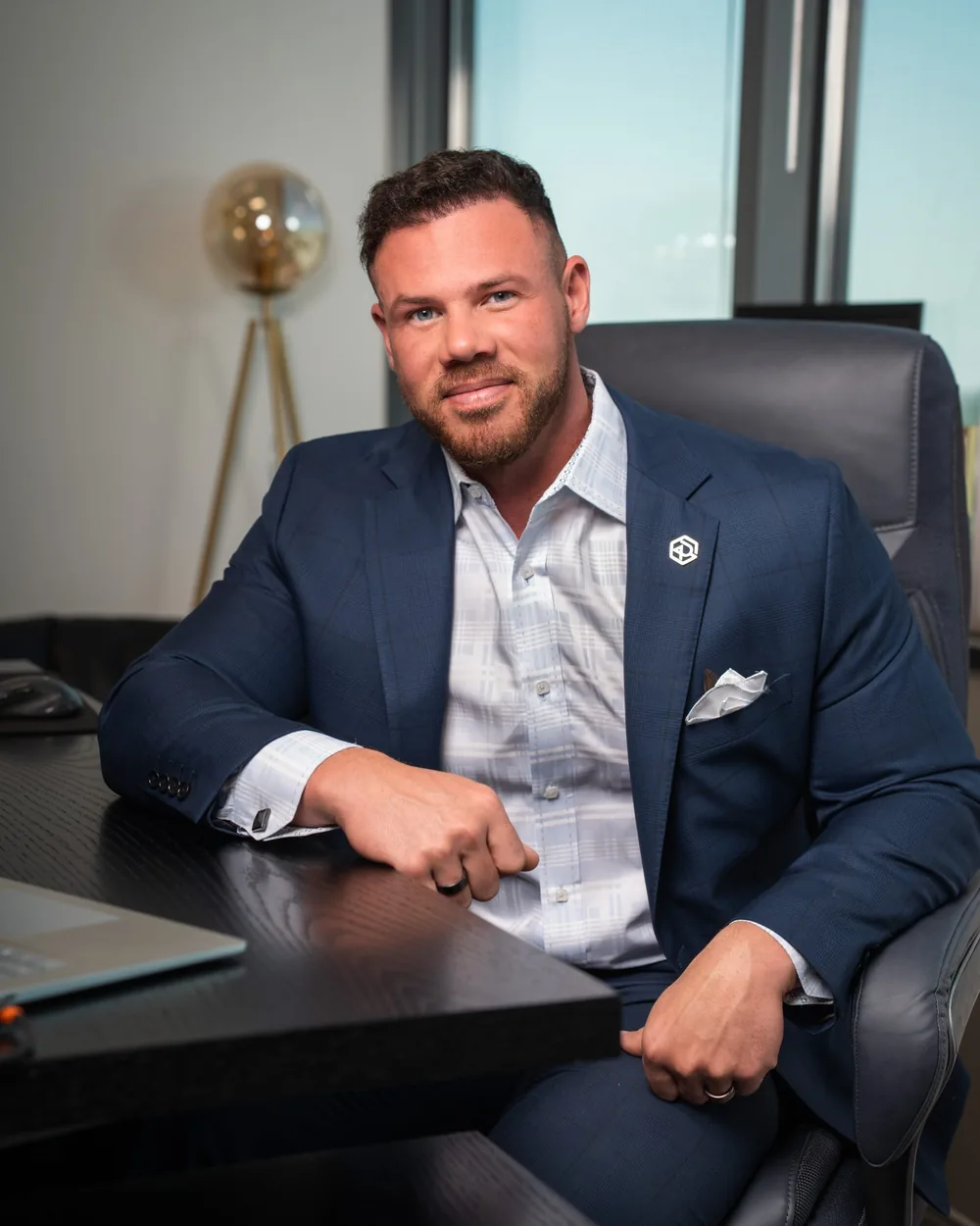 Jake Claver seated at a desk in a navy suit